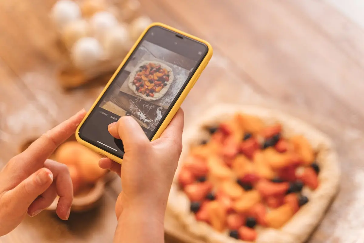Mains photographiant une tarte aux fruits avec un smartphone pour les réseaux sociaux