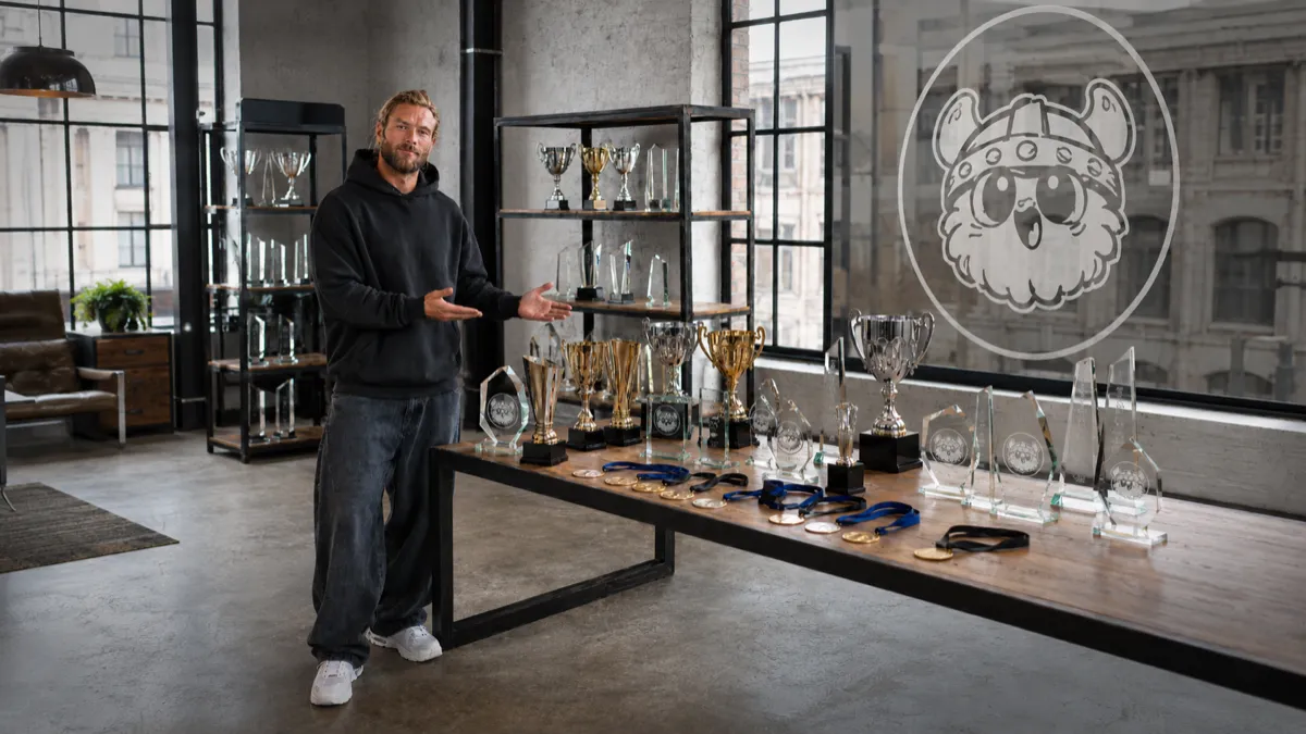 Homme présentant une collection de trophées, coupes et médailles avec le logo Vik de GLAAZ en arrière-plan